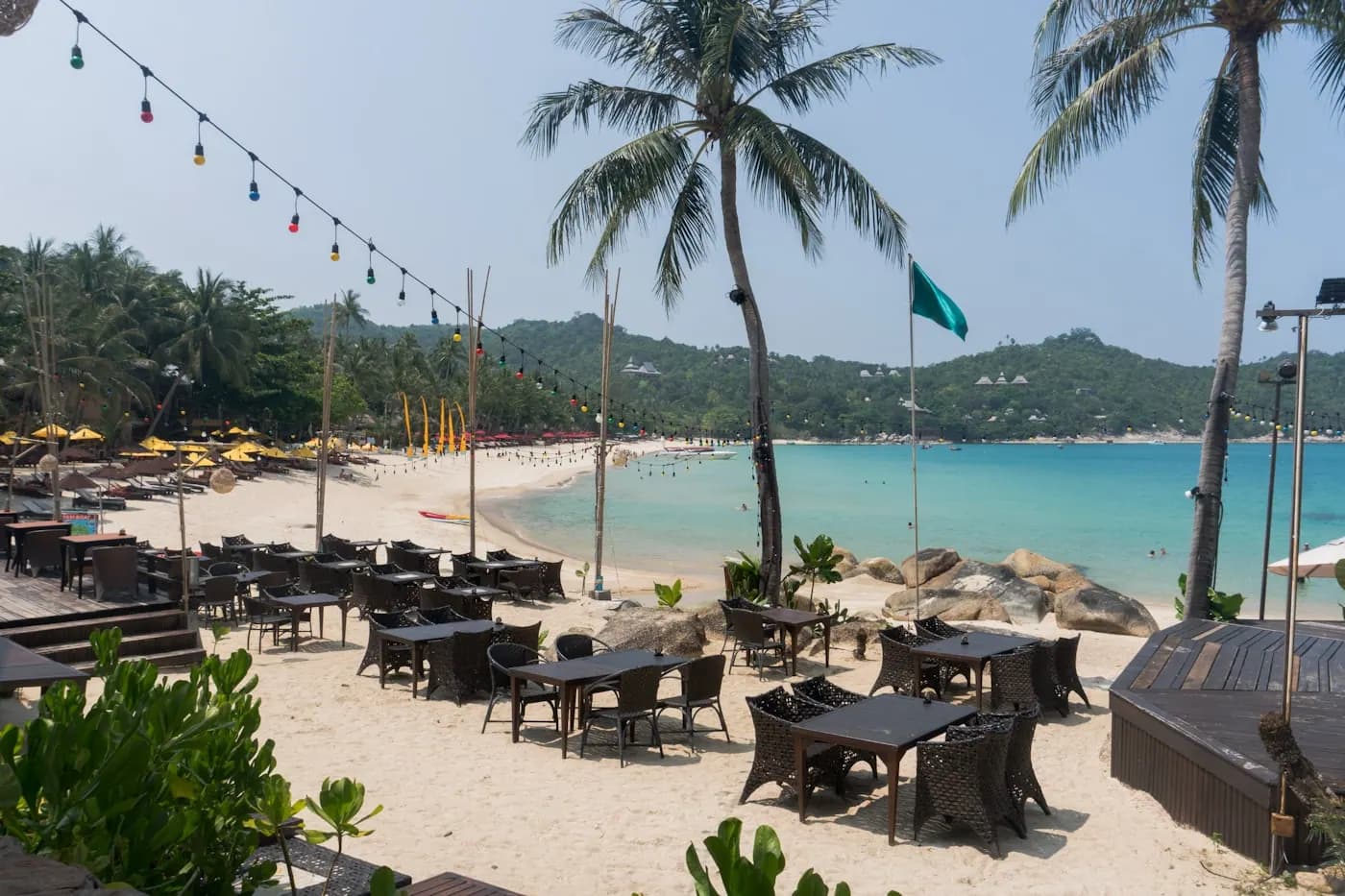 Restaurant tables and umbrellas set out on a beach under palms