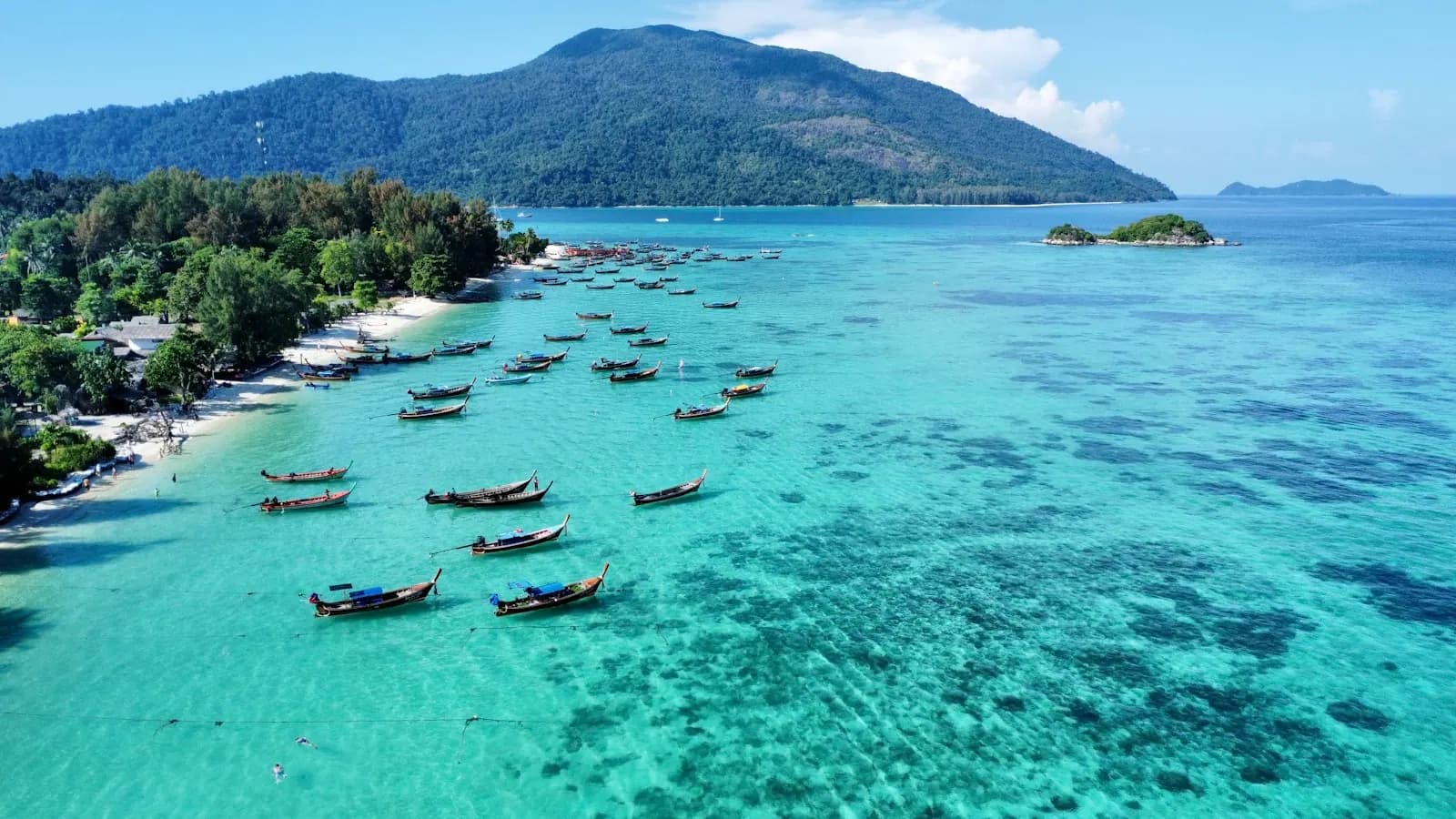 Longtail boats moored over turquoise water beside a white-sand beach